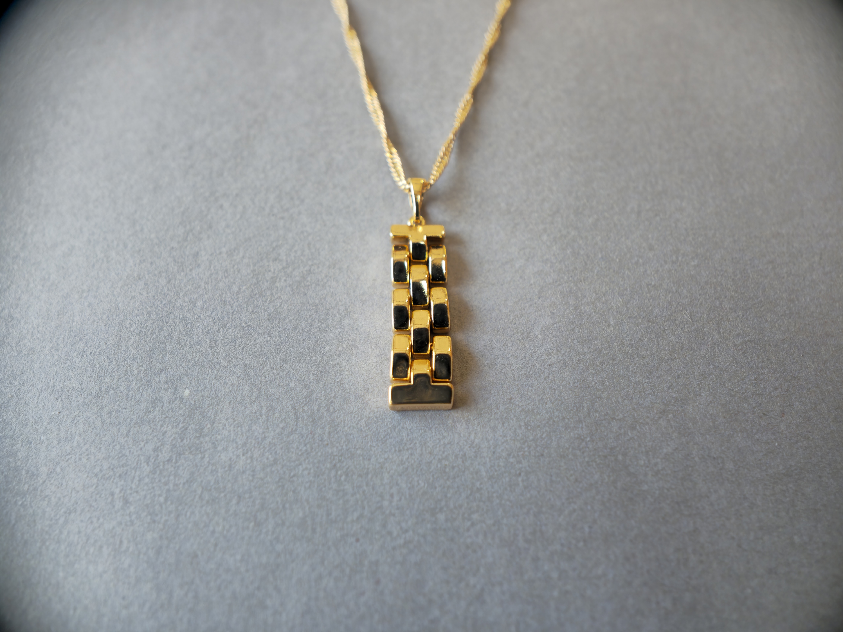 Dije dorado con cadena sobre una superficie gris clara.