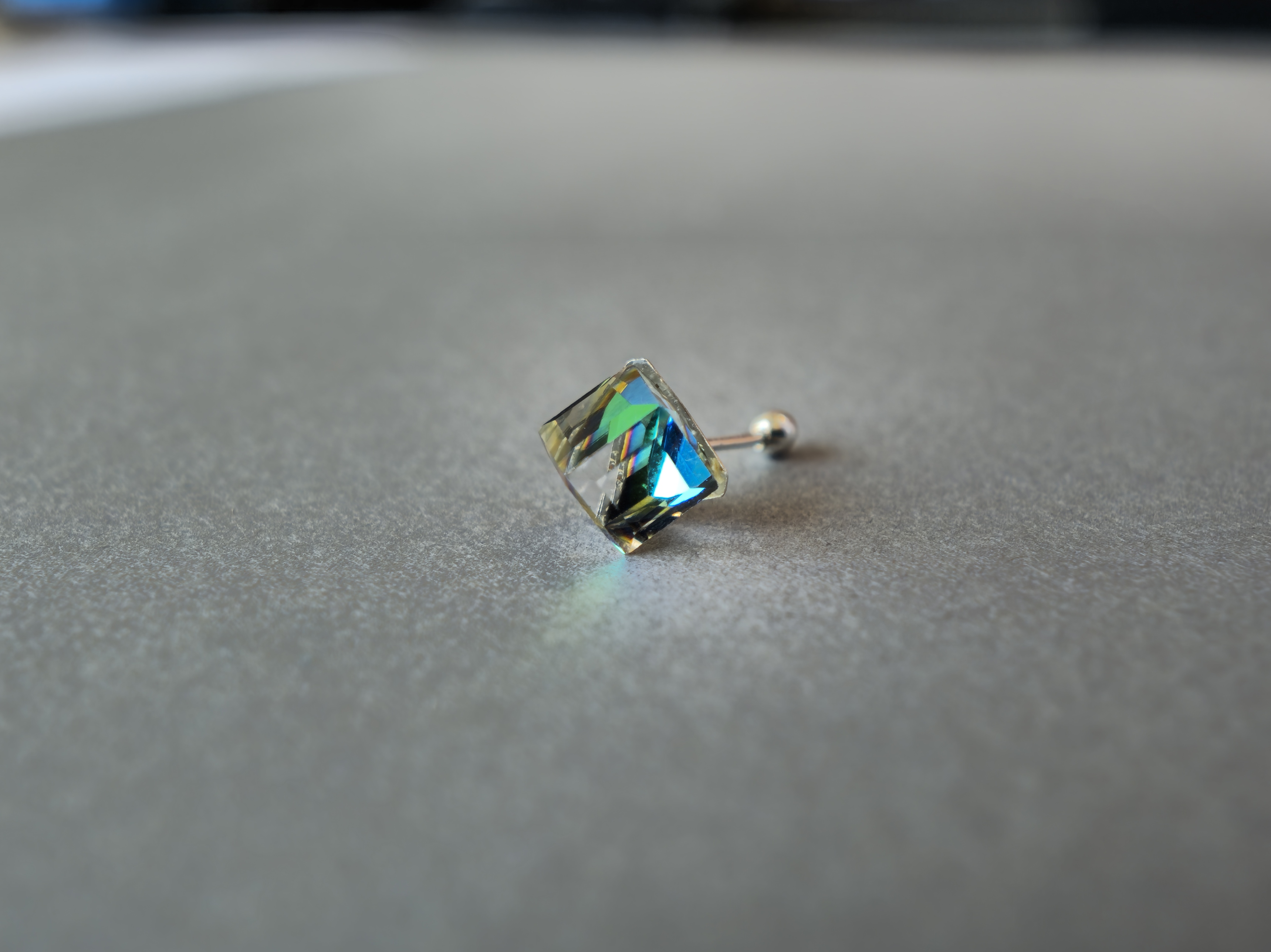 Arete cuadrado con reflejos iridiscentes sobre una superficie gris clara.