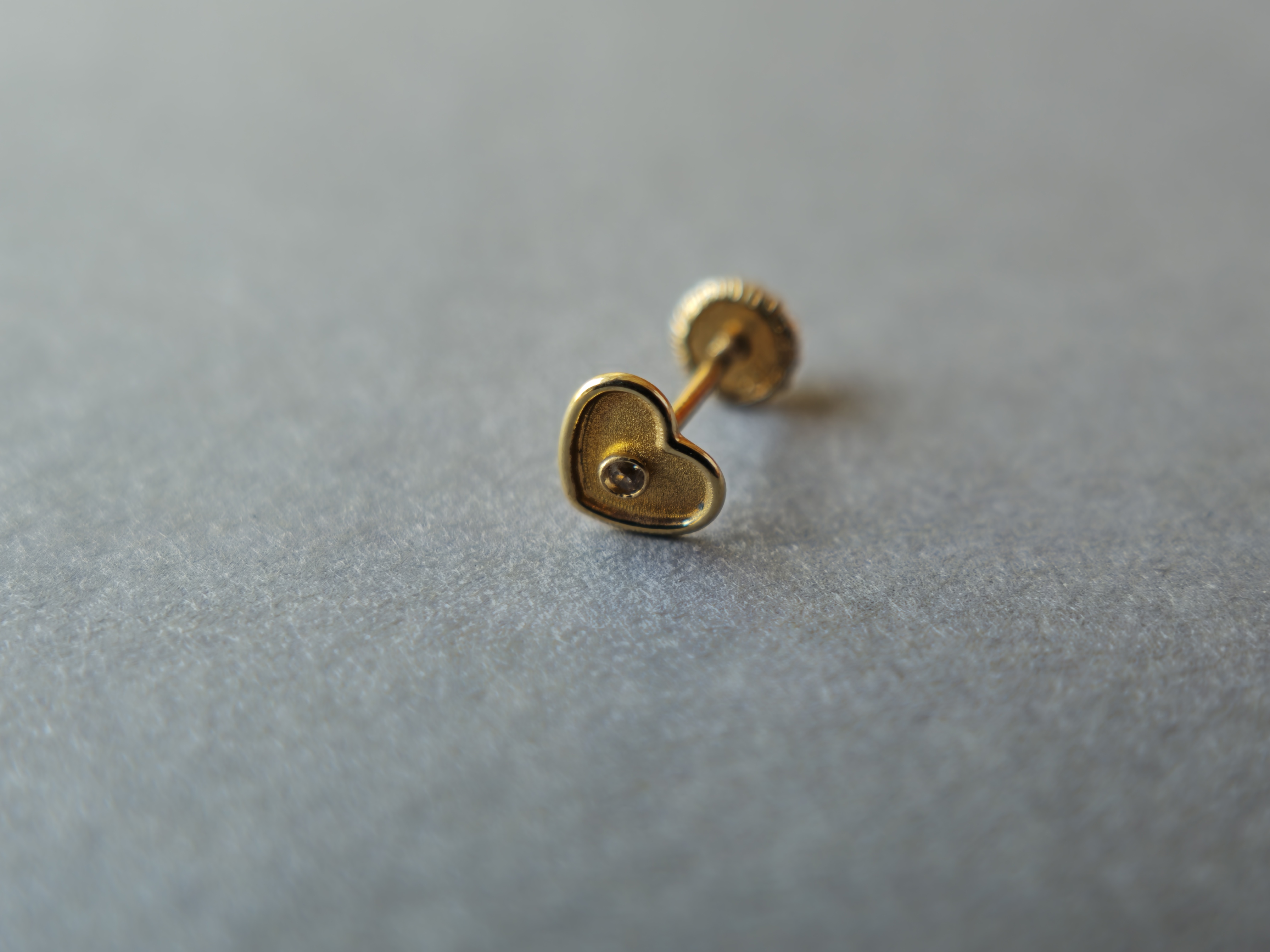 Arete dorado en forma de corazón sobre una superficie gris clara.